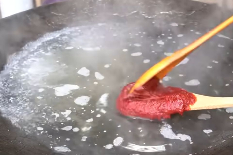 Cho tương ớt và bột ớt vào nước dùng đang nấu
