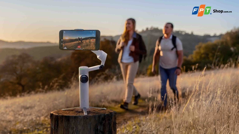 Điện thoại gắn trên gimbal đặt trên gốc cây để ghi hình hai người đi bộ ngoài trời