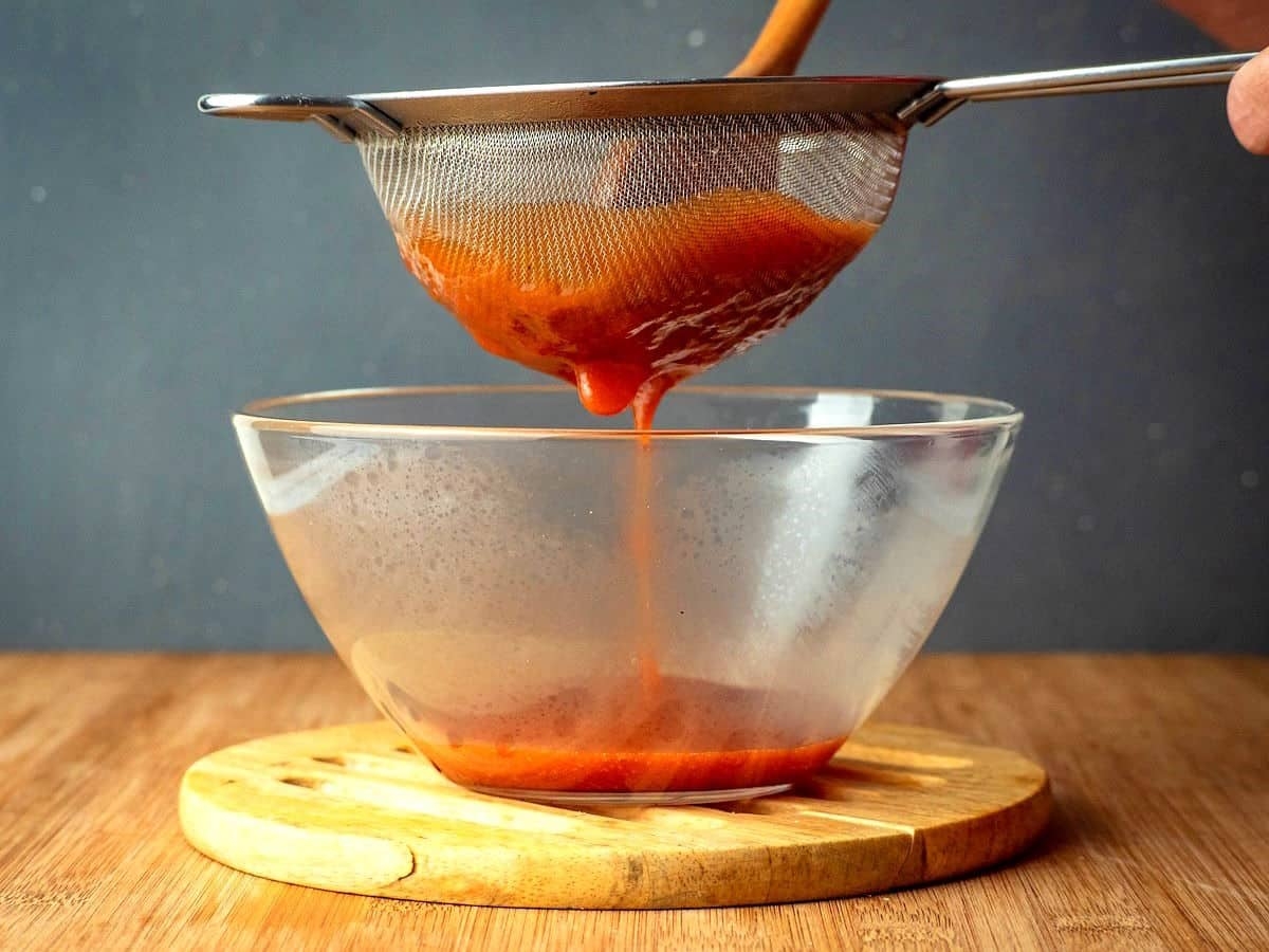 Lọc hỗn hợp đã xay nhuyễn qua rây lưới mịn, dùng thìa ấn xuống để chiết được càng nhiều hỗn hợp cà chua càng tốt.