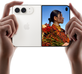 iPhone Duo, màu Trắng Ánh Sao, được cầm bằng hai tay theo hướng ngang, đang mở ra, màn hình bên trái hiển thị camera sau Dual Fusion 48MP, màn hình bên phải hiển thị một người đang chụp ảnh trên màn hình ngoài, chủ thể trong ảnh chụp có thể nhìn thấy khuôn mặt của chính mình khi ảnh được chụp bằng tính năng Duo Preview